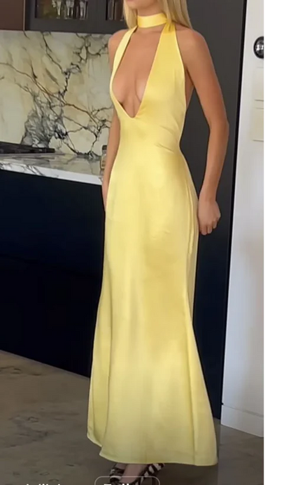 Model wearing a daring yellow satin mermaid prom dress with deep-plunge halter neckline and open back.