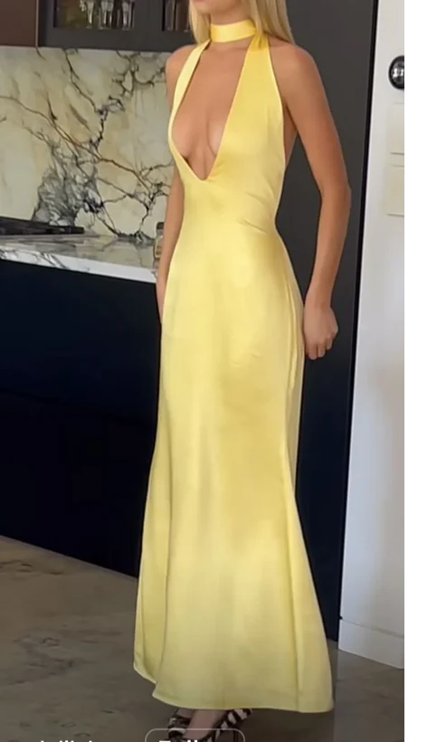 Model wearing a daring yellow satin mermaid prom dress with deep-plunge halter neckline and open back.