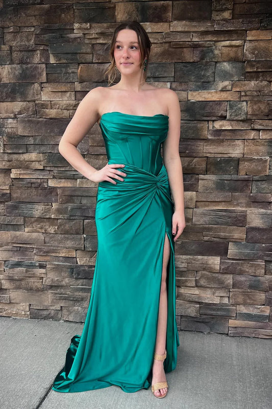 Model wearing a strapless draped satin mermaid prom dress with a high slit and lace-up back.