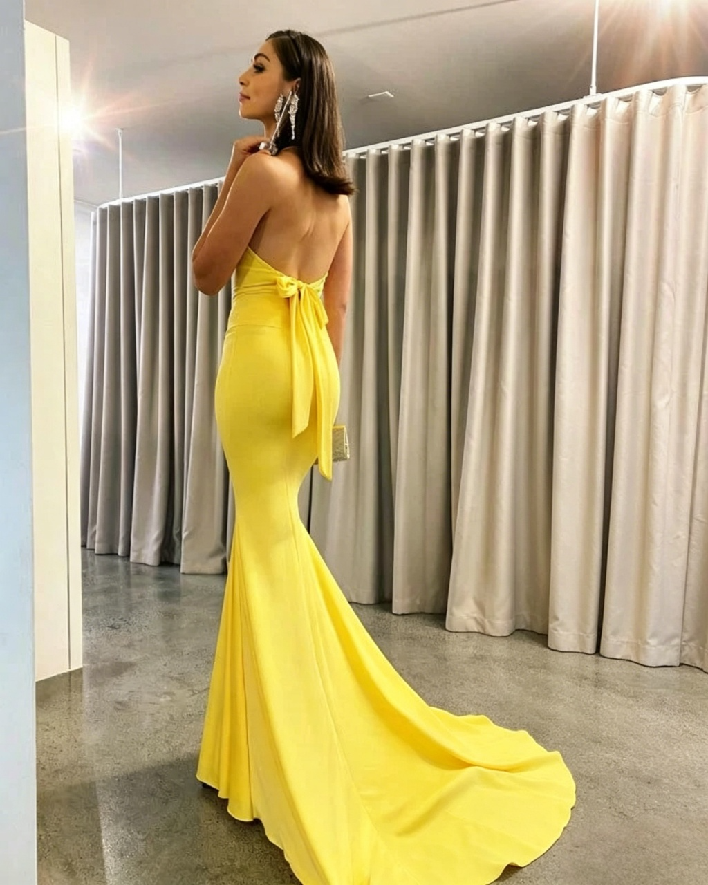 Back view of yellow mermaid prom dress showing large open-back bow detail.