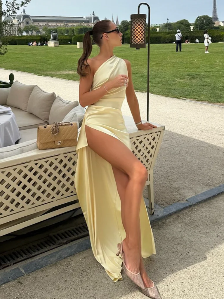 Woman in elegant satin mermaid one-shoulder prom dress with open back and high slit, front view.