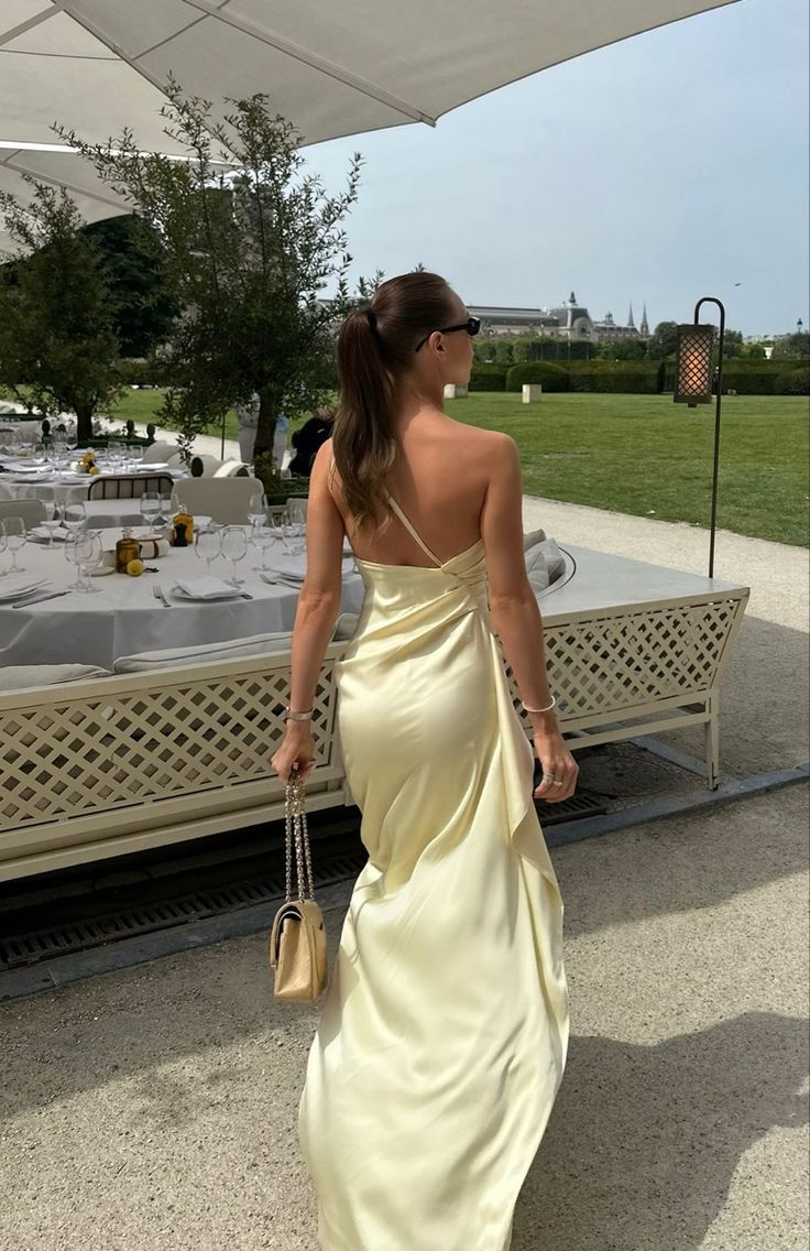 Woman in elegant satin mermaid one-shoulder prom dress, side view showing high slit.