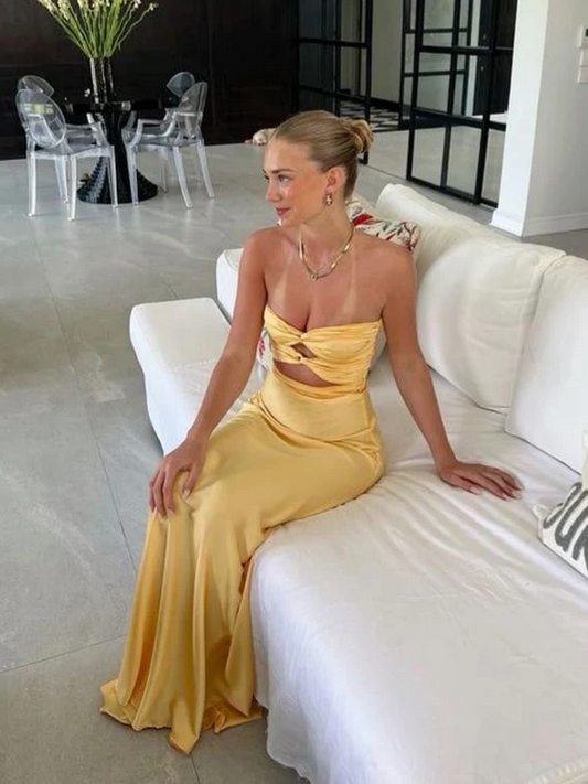 Model wearing a yellow satin mermaid prom dress with a strapless twist bodice and midriff cutout.