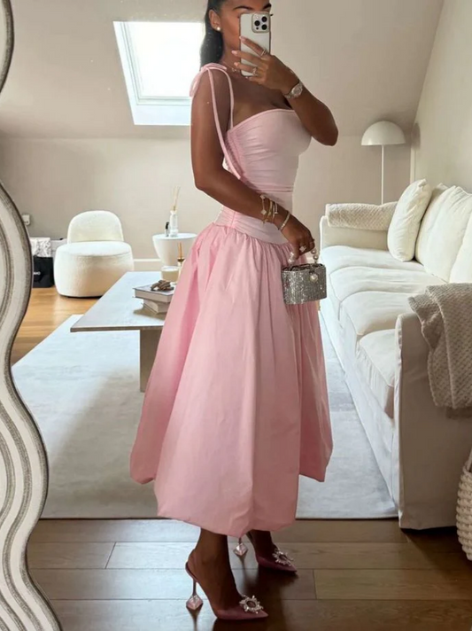 Model wearing a pink A-line midi prom dress with strapless tie-shoulder and ruched bodice.