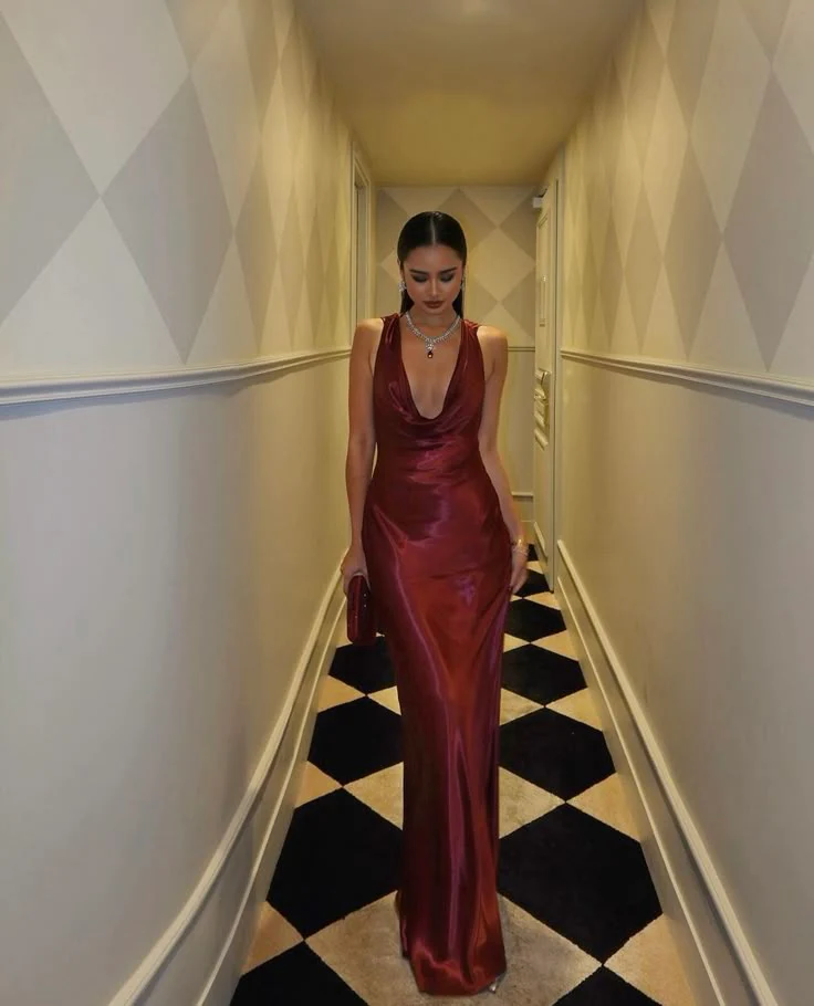 Model wearing a regal satin mermaid prom dress with cowl neck and open back, front view.